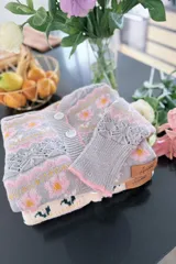 Saco de punto con diseño floral, cuello redondo y cierre frontal con botones. Presenta detalles de tejido calado en las mangas y puños acanalados. Incluye etiqueta de cuero sintético con la marca Amante.