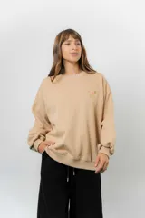 Buzo oversize de algodón frizado color beige, con cuello redondo, puños y cintura tejidos. Presenta un bordado pequeño de Snoopy en el frente.