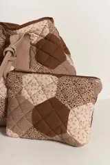 Bolso tipo tote amplio, confeccionado en patchwork de hexágonos con diferentes estampados en tonos azul marino y blanco/gris. Presenta asas y base en tela lisa gris. El cuerpo del bolso tiene un efecto acolchado.