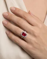Anillo de plata con piedra central rectangular de rubí en corte esmeralda, rodeada por un pavé de circonias cúbicas y detalles en los laterales.