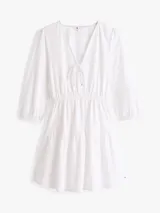 Vestido corto blanco de popelina de algodón, con escote en V, mangas 3/4 abullonadas y falda escalonada con volantes.