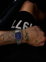 Reloj Casio con caja cuadrada de bordes redondeados, esfera azul vibrante con índices plateados y ventana de fecha. Cuenta con malla de eslabones de acero inoxidable y movimiento de cuarzo.