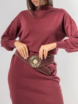 Faja de gamuza color bordó con tachas metálicas doradas en los bordes y hebilla circular grande con diseño calado y piedra central.