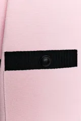 Chaqueta de punto rosa con ribetes negros en el cuello, la botonera, los bolsillos, los puños y el ruedo. Cuenta con manga corta, cuello redondo, bolsillos frontales de plastrón con botones y cierre frontal abotonado.