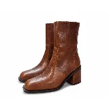 Bota de caña media confeccionada en cuero vacuno color marrón, con punta cuadrada y taco de madera. Presenta un diseño minimalista con cierre lateral interno y elástico en la caña para un mejor ajuste.