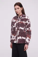 Campera tipo camisa de manga larga con cierre frontal de botones metálicos, bolsillos frontales con solapa y diseño estampado tipo tie-dye en tonos marrones y blancos.