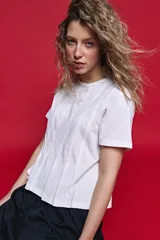 Remera de algodón color blanco con diseño de tablas verticales en el frente que aportan movimiento y estructura.