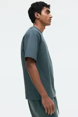 Remera verde oscuro de corte relajado, confeccionada en punto de algodón de peso medio, con cuello redondo ribeteado y hombros caídos.
