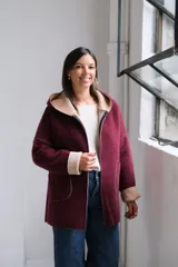 Tapado de paño bordó con interior en color beige, diseño con capucha, cierre frontal y bolsillos laterales. Presenta costuras visibles y puños vueltos que dejan ver el contraste de color.