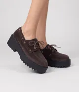 Mocasín de cuero con acabado en gamuza color marrón, estilo desert shoe, con cordones frontales, ojales dorados y suela flatform alta y track de color negro.