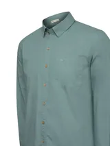 Camisa de manga larga color verde menta, confeccionada en popelina 100% algodón orgánico. Presenta cuello camisero, botones de madera, un bolsillo de parche en el pecho con logo bordado y presillas con botón en las mangas para sujetarlas enrolladas.