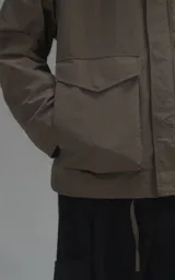 Campera técnica liviana color beige, confeccionada en microfibra de alta densidad con acabado mate. Presenta mangas desmontables que permiten convertirla en chaleco, cuello tipo camisa, cierre frontal oculto bajo cartera y logo bordado en el pecho. Incluye cuatro bolsillos frontales de gran tamaño con solapa y puños con elástico.