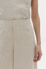 Pantalón ancho color beige confeccionado en lino 100% natural, de tiro medio-alto con elástico interno en la cintura, cierre frontal con gancho y bolsillos laterales.