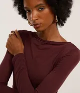Blusa de punto de viscosa color bordó, con cuello asimétrico ceñido al cuello, mangas largas y fruncido lateral.