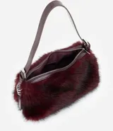 Cartera mediana de pelo sintético color bordó, con asa única de cuero sintético brillante, cierre superior por cremallera y detalles de argollas metálicas en los laterales.
