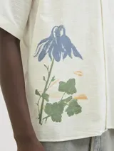 Camisa de algodón color crudo con estampado de flores y billetes, cuello resort, calce relajado, mangas cortas y cierre de botones.