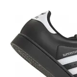 Championes Adidas modelo Superstar, color negro con las icónicas tres rayas laterales y detalle en el talón en color blanco. Presenta la clásica puntera de goma con relieve y suela negra.