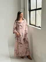 Vestido largo rosado con estampado floral en tonos marrones y beige, cuello drapeado y mangas largas holgadas.