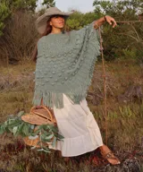 Poncho de lana merino color marfil, tejido a mano con diseño de puntos en relieve y largos flecos en los bordes.
