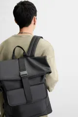 Mochila verde militar con acabado engomado, solapa superior con cierre de hebilla y cremallera, bolsillo frontal con cierre imantado, compartimento interno para laptop de hasta 13 pulgadas, asa de mano superior, correas de hombro ajustables y espalda acolchada. Base de cuero sintético negro.