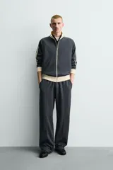 Sudadera de corte relajado en color azul marino con cuello alto y cierre frontal de cremallera. Presenta bandas laterales en color crema a contraste que recorren las mangas, puños y bajo en tejido rib, y bolsillos laterales de vivo.