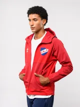 Campera deportiva Umbro del Club Nacional de Football, modelo Summit. Presenta un diseño con bloques de color en azul, rojo y blanco, con capucha, cierre frontal y bolsillos laterales con cierre. Incluye el logo de la marca y el escudo del club en el pecho.