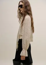 Blusa de gasa color beige con estampado de lunares negros, cuello alto con lazo integrado y mangas largas con puños amplios.