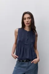 Blusa sin mangas color negro, de silueta fluida, con cuello redondo, detalle de alforzas en el frente y abotonadura parcial con botones visibles.
