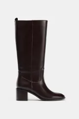 Bota alta de caña media en color marrón oscuro, con diseño minimalista, punta redonda y tacón bloque de madera. Cuenta con tirador trasero para facilitar el calce.