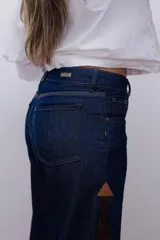 Pantalón de jean estilo wide leg, confeccionado en denim rígido de color azul oscuro. Presenta paneles laterales de encaje con diseño floral en tono rojizo y terminaciones deshilachadas en el ruedo.