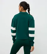 Saco deportivo de modal color verde, con cuello polo, escote en V y mangas largas con franjas blancas horizontales. Presenta un bordado circular en el pecho con la inscripción '94'.