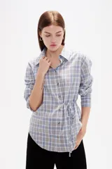 Camisa de poliéster con estampado a cuadros, cuello camisero, cierre frontal con botones y detalle de lazo ajustable en la cintura.