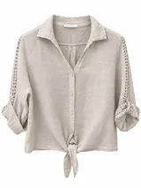 Camisa beige de lino con mangas largas y detalles perforados, cuello camisero, cierre frontal con botones y nudo ajustable en la parte inferior.
