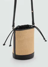 Bolso tipo bucket de tamaño pequeño con cuerpo de rafia y detalles en cuero sintético negro. Cuenta con asa de mano fija, correa bandolera ajustable y extraíble, y cierre superior.