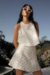 Conjunto de dos piezas compuesto por un top sin mangas de corte holgado y una falda corta acampanada, ambos confeccionados en lino con estampado de lunares dorados.