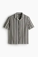 Camisa de manga corta con cuello abierto, confeccionada en tejido texturizado con diseño de rayas verticales en tonos oscuros y claros. Presenta un corte regular fit, tapeta frontal con botones y bajo recto.