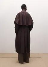 Chaqueta larga tipo gabardina color marrón oscuro, de diseño recto, con solapas amplias y cinturón ajustable del mismo tejido.
