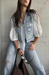 Chaleco de denim celeste con bordados detallados y apliques de brillos en la parte frontal.