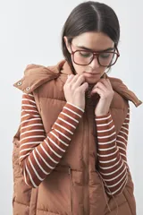 Chaleco puffer negro con diseño acolchado, capucha desmontable y cierre frontal. Cuenta con cordones ajustables en la cintura y bolsillos laterales.