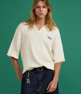 Camisa polo oversized de punto color marfil, de manga corta y cuello en V, con estampa lettering "Newport Breeze" en el pecho.