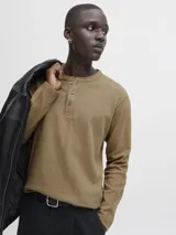 Camiseta de manga larga con cuello henley y cierre frontal de tres botones. Confeccionada en algodón orgánico de textura suave, presenta un corte regular y diseño clásico.