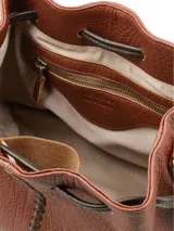 Cartera tipo morral de cuero graneado color marrón terracota, con formato de saco fruncido mediante tiras ajustables oscuras. Presenta una costura decorativa central con tientos a contratono y correa regulable.
