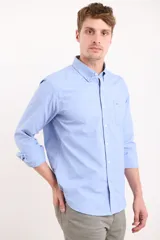 Camisa celeste con cuello abotonado, manga larga con puños abotonados y bolsillo en el pecho.