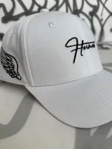 Gorro blanco con visera, con bordado de ala en el lateral y texto en el frente.