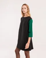 Vestido corto negro con mangas 3/4 verdes, cuello bote y bolsillos laterales.
