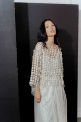 Blusa de red en color blanco con apliques de flores tridimensionales en toda la prenda. Presenta transparencias, cuello redondo y mangas largas.