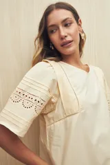 Vestido corto color crema, de corte recto y cuello redondo. Presenta mangas cortas amplias con calados geométricos en el ruedo.