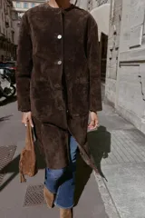 Abrigo de piel color marrón, con cuello redondo, manga larga, cierre frontal con botones y dos bolsillos delanteros de plastrón.