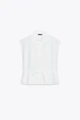 Camisa blanca de popelín con cuello solapa, manga sisa y detalle de guipur floral en el frente. Incluye un cinturón fino del mismo tejido que se ata en la cintura.