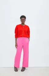 Cárdigan de punto rojo con cuello redondo, cierre frontal de botones y mangas largas con puños ajustados. Presenta un diseño de corte holgado y textura esponjosa.